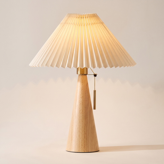 Natural wood pleated table lamp switched on with a cream pleated shade and a brass pull chain