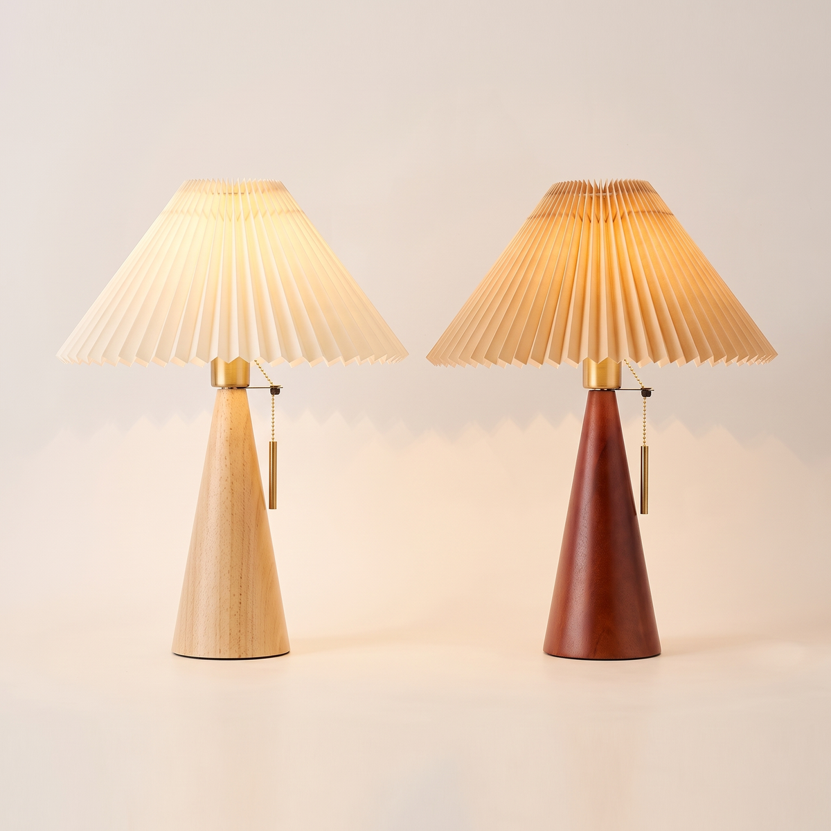 Two pleated table lamps side by side, natural wood with cream shade and walnut wood with beige shade