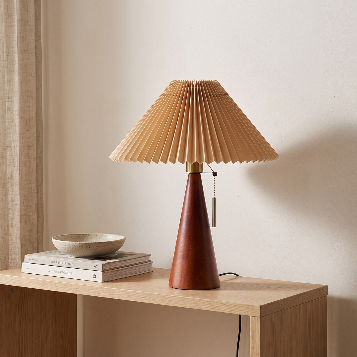 Walnut pleated table lamp switched off on a pale oak console beside books and a ceramic bowl
