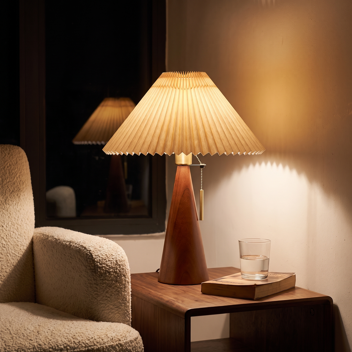 Living room corner at night lit only by the walnut pleated table lamp on a side table