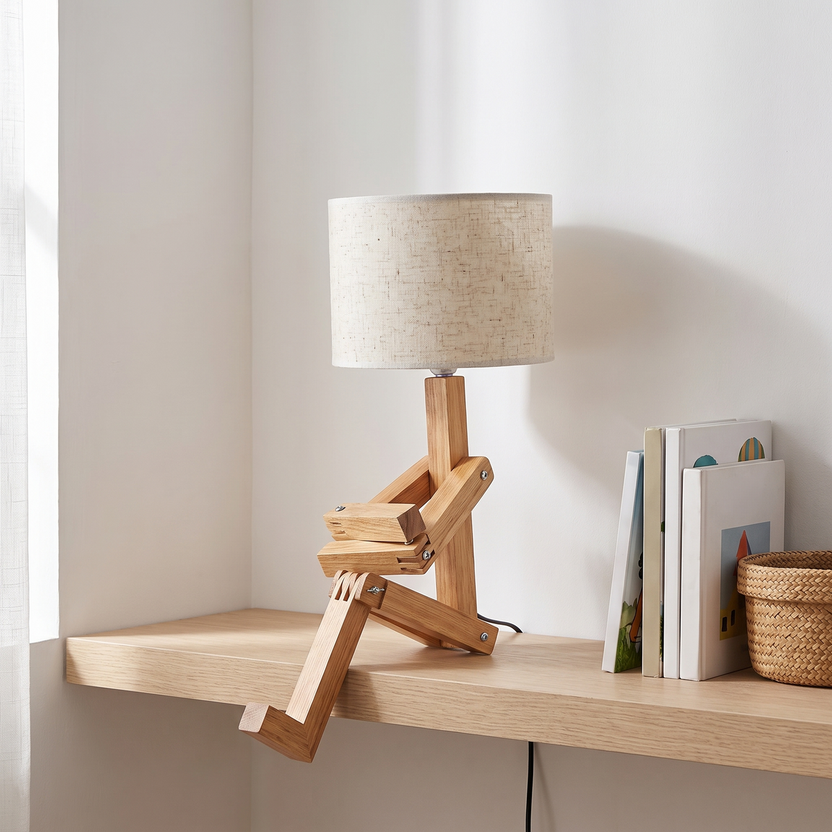 Jointed wooden robot desk lamp with a beige shade on a child's bookshelf in daylight