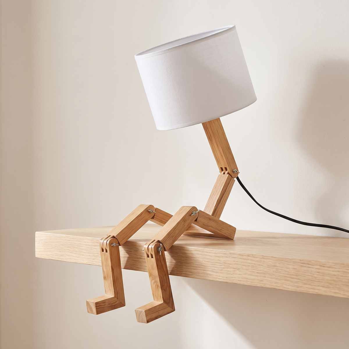 Jointed wooden robot desk lamp posed leaning back with its legs over the edge of a shelf