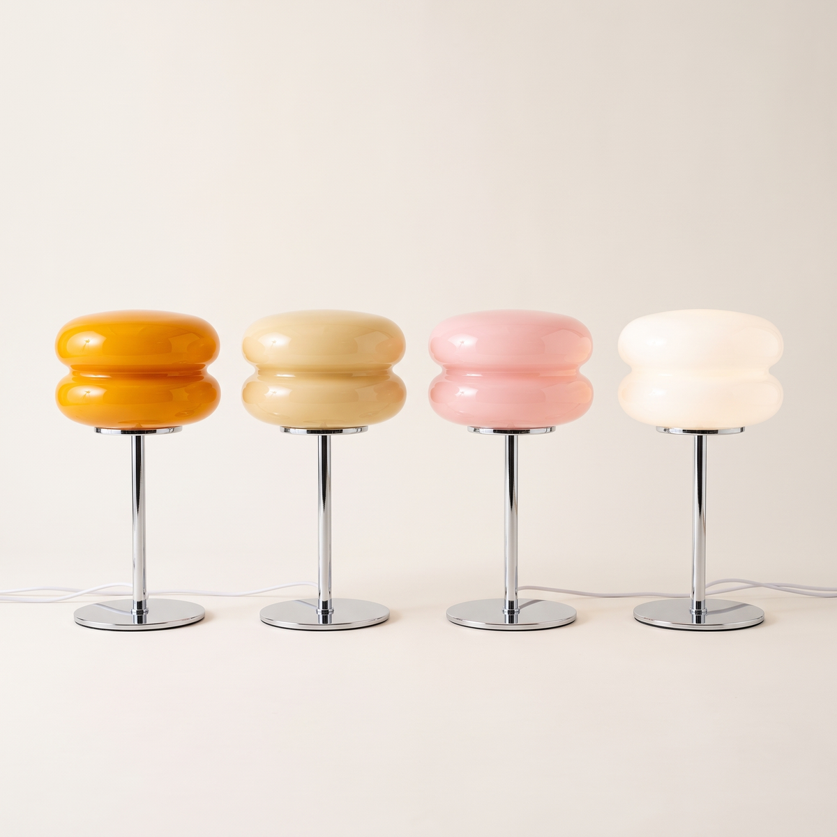 Four macaron glass table lamps in a row in orange, beige, pink and white on chrome stems