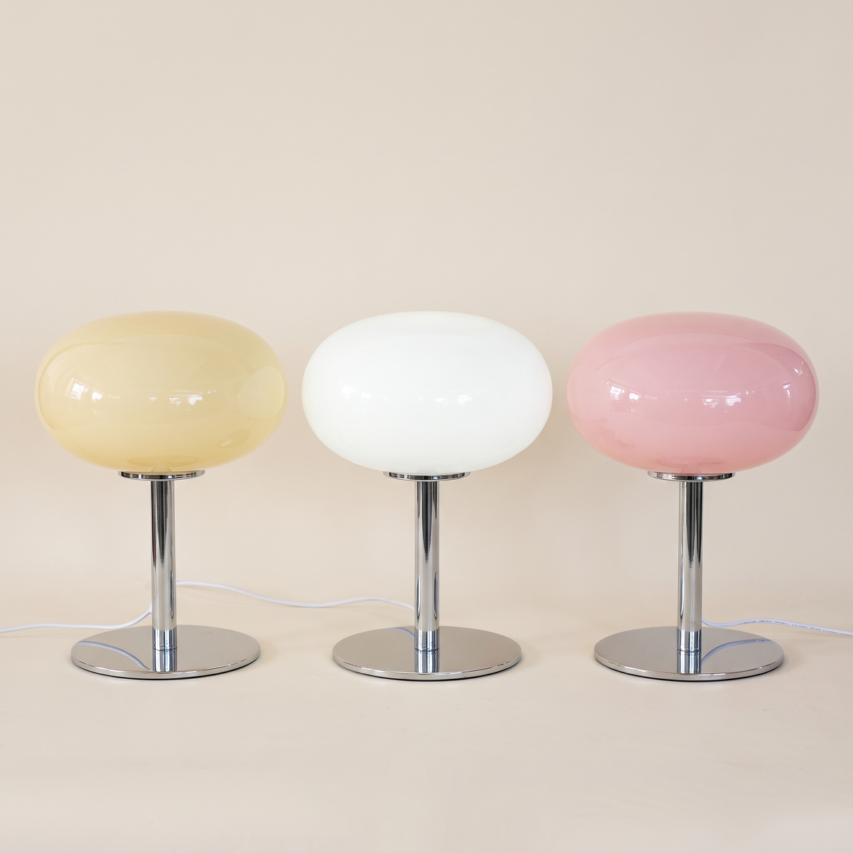 Three snowball glass table lamps in a row in cream, white and pink on chrome stems