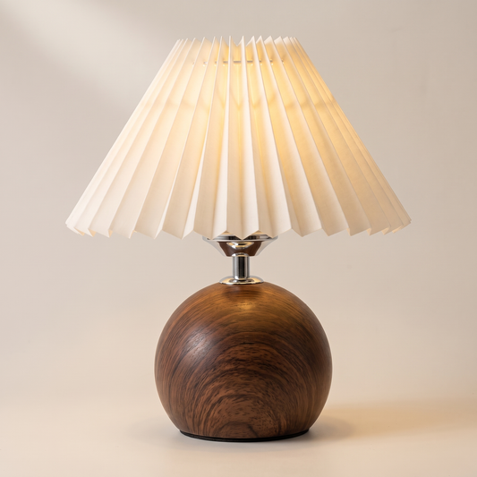 Small wooden ball table lamp in dark walnut with an off-white pleated shade, switched on