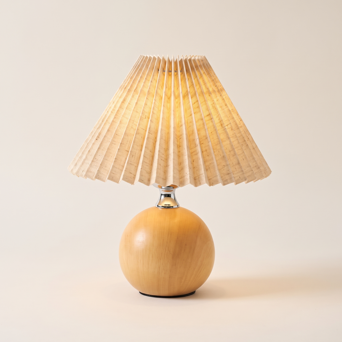 Light wood ball table lamp with an oatmeal linen pleated shade, switched on