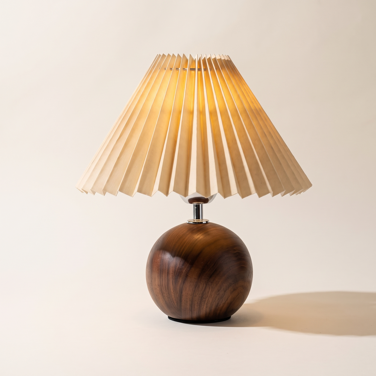 Dark walnut ball table lamp with a warm beige pleated shade, switched on