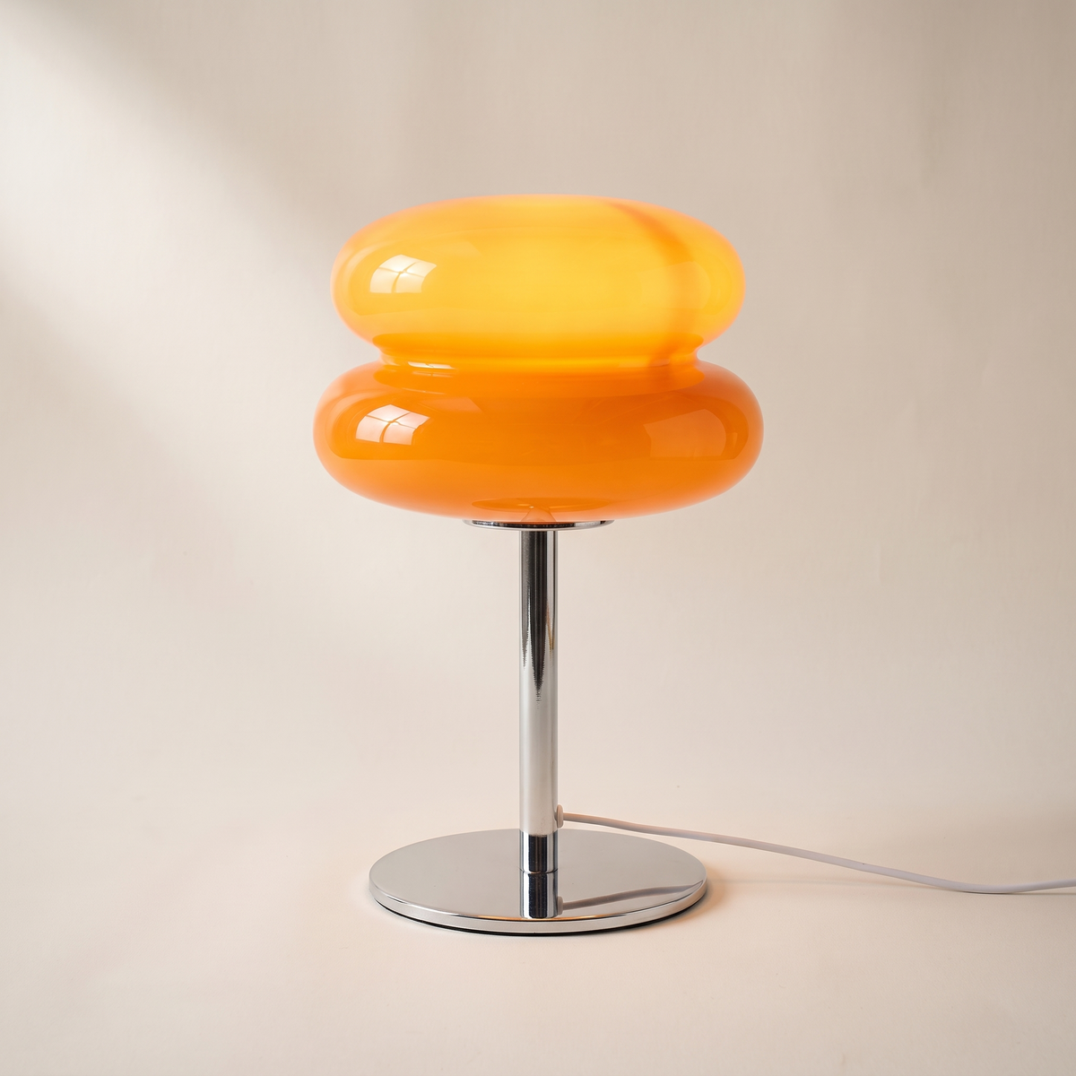 Orange glass table lamp with two stacked macaron tiers on a chrome stem, switched on