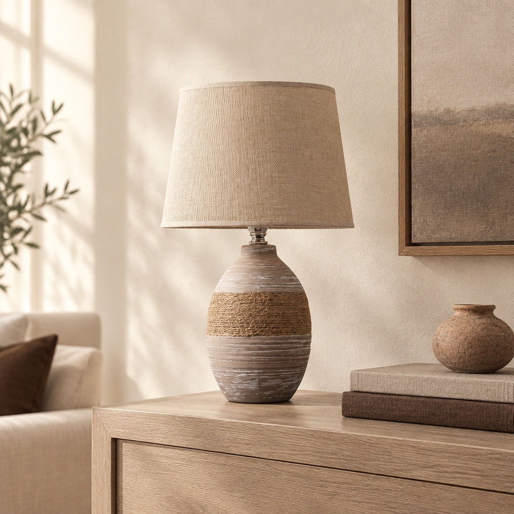 Taupe ceramic table lamp switched off on a pale oak console beside books and a clay vessel