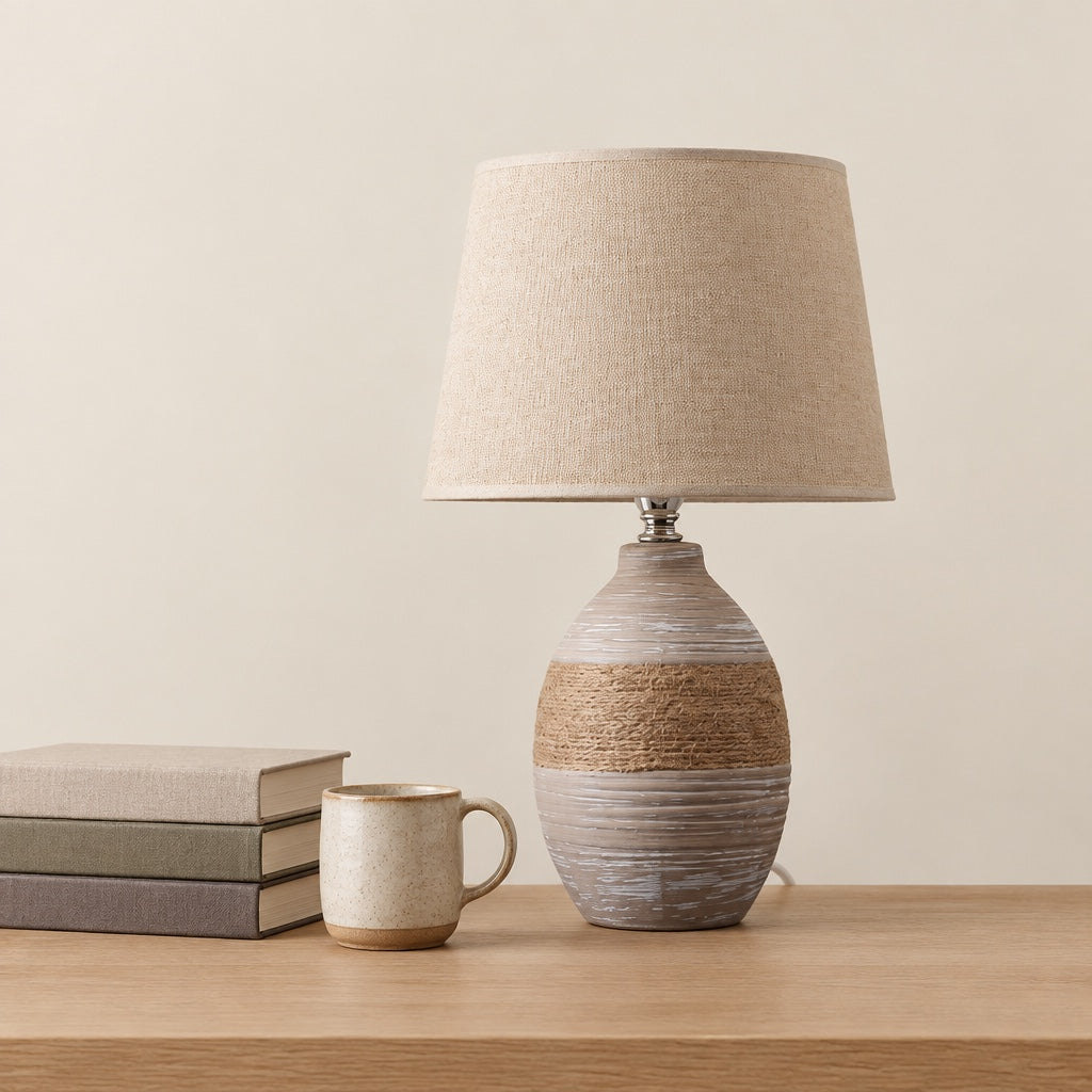 Taupe ceramic table lamp beside a stack of books and a stoneware mug showing its size